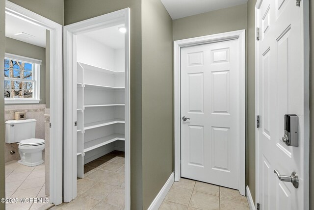 bathroom featuring toilet, wainscoting, tile patterned flooring, and tile walls