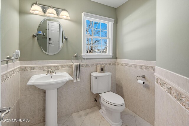 half bathroom with toilet, tile patterned flooring, tile walls, and wainscoting