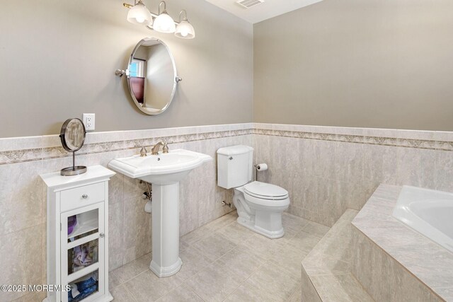 bathroom with tile patterned flooring, toilet, visible vents, wainscoting, and tiled tub