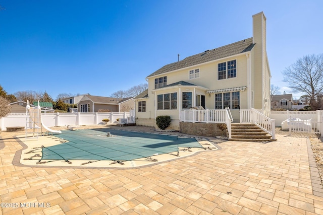 rear view of property with a deck, a fenced backyard, a fenced in pool, a chimney, and a patio area