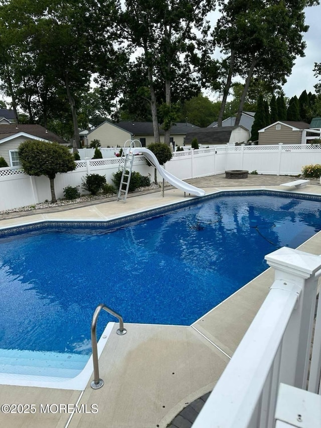 view of pool with a diving board, a water slide, a fenced backyard, and a fenced in pool