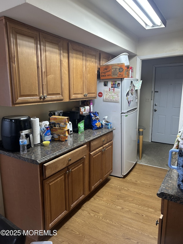 kitchen featuring dark stone countertops, brown cabinets, freestanding refrigerator, and light wood-style floors