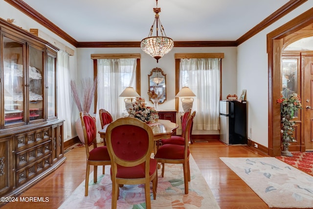 dining room featuring light wood-style floors, baseboards, crown molding, and an inviting chandelier