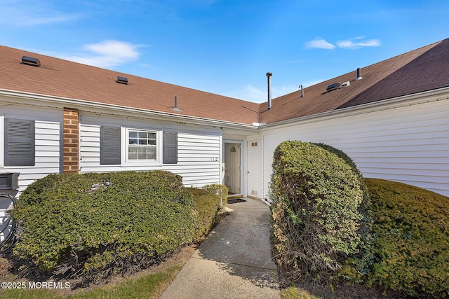 entrance to property featuring brick siding and a shingled roof