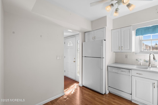 kitchen with backsplash, wood finished floors, white cabinets, white appliances, and a sink