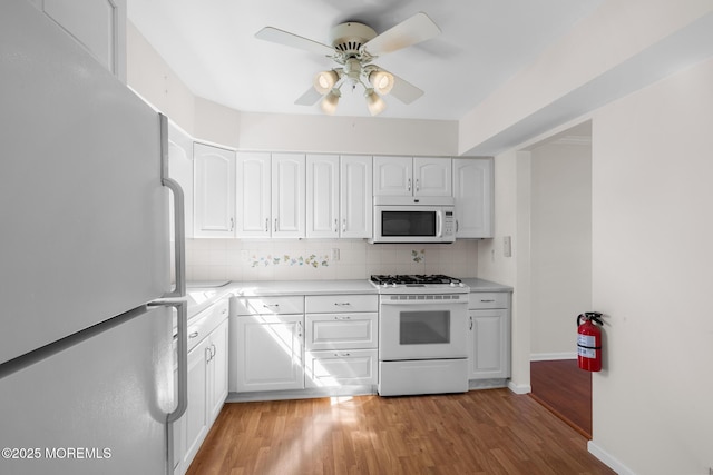 kitchen featuring white appliances, ceiling fan, decorative backsplash, light countertops, and light wood-style floors