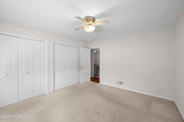 unfurnished bedroom with visible vents, two closets, carpet floors, baseboards, and ceiling fan