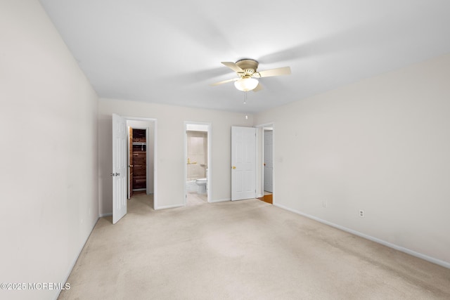 unfurnished bedroom featuring a closet, light colored carpet, a walk in closet, and baseboards