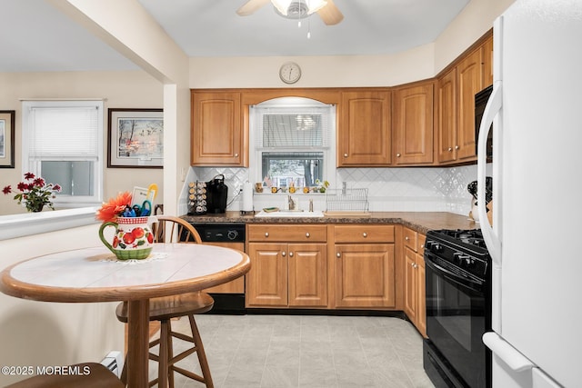 kitchen with tasteful backsplash, black gas range oven, brown cabinetry, freestanding refrigerator, and dishwashing machine