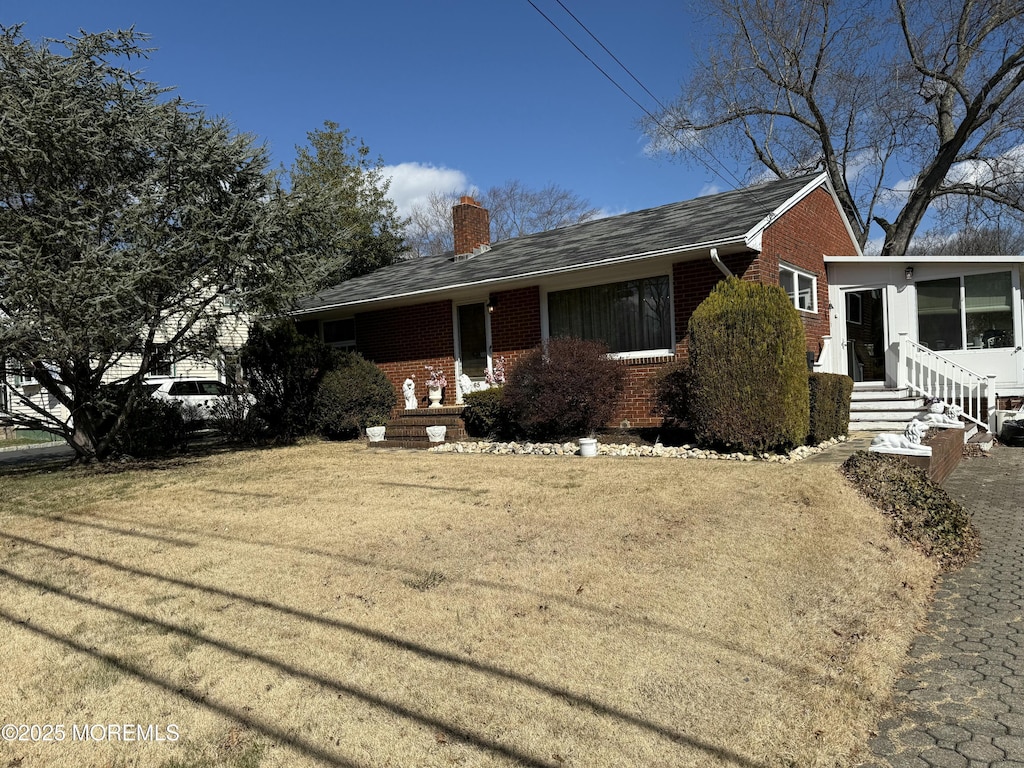 ranch-style home featuring brick siding, a chimney, and a front yard