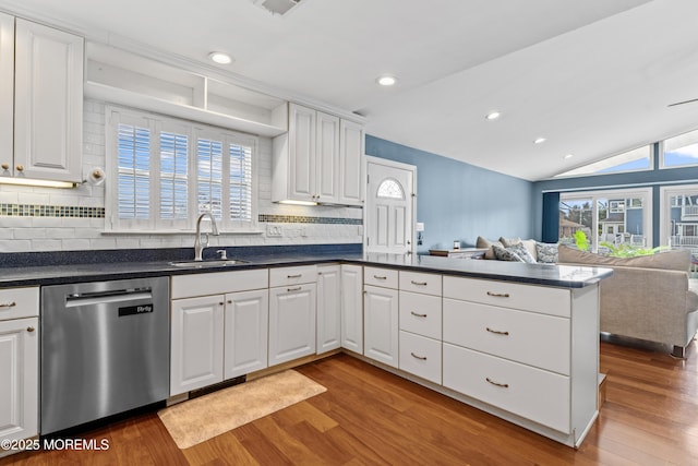 kitchen with a peninsula, a sink, open floor plan, stainless steel dishwasher, and dark countertops