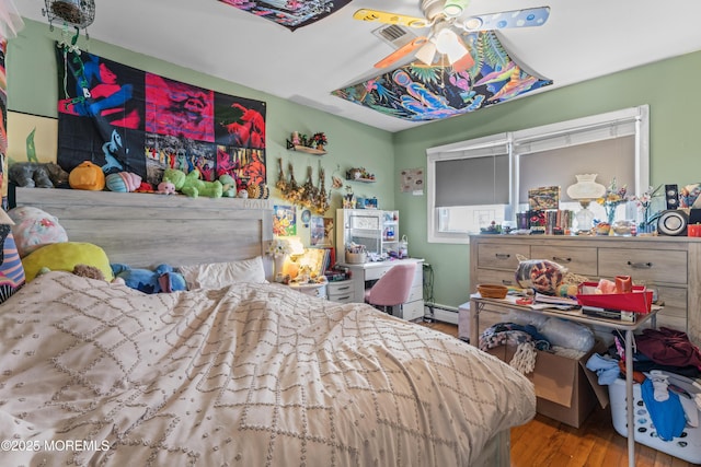 bedroom with a ceiling fan, visible vents, baseboard heating, and wood finished floors