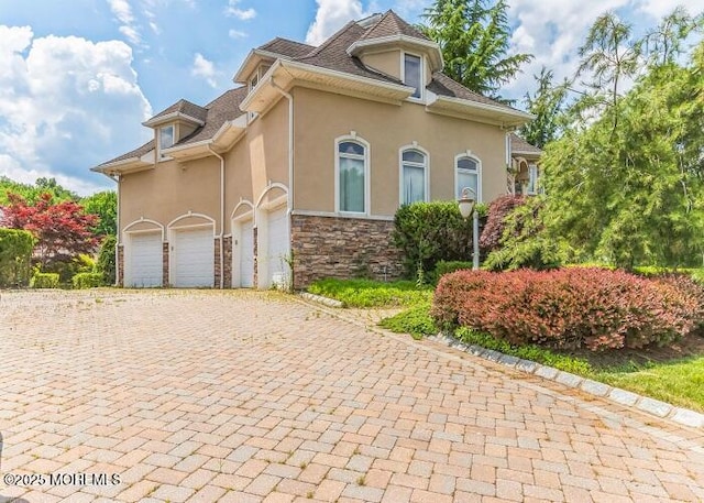 view of side of home featuring stone siding, stucco siding, and decorative driveway