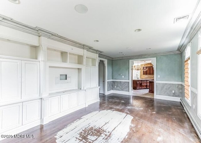 unfurnished room featuring wood finished floors, visible vents, wainscoting, crown molding, and baseboard heating