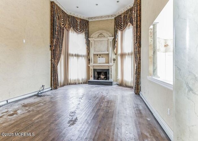 unfurnished living room with baseboards, baseboard heating, a fireplace with raised hearth, and wood finished floors