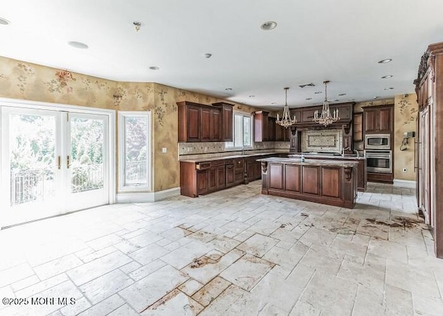 kitchen featuring a center island, light countertops, an inviting chandelier, stone tile flooring, and stainless steel appliances