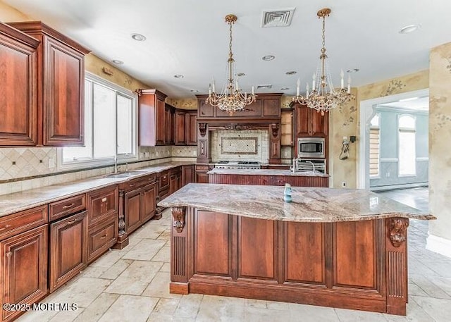 kitchen with stainless steel microwave, visible vents, a chandelier, a center island with sink, and a sink