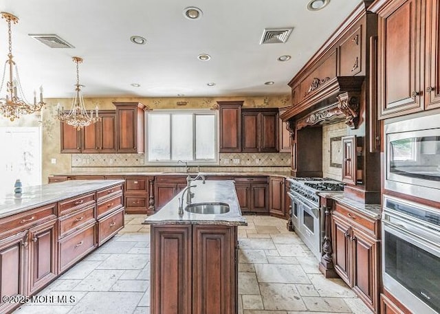 kitchen with visible vents, a kitchen island with sink, stone tile flooring, a sink, and appliances with stainless steel finishes