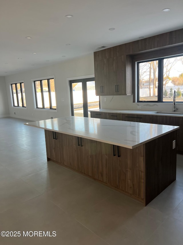 kitchen with light stone counters, a spacious island, recessed lighting, a sink, and modern cabinets