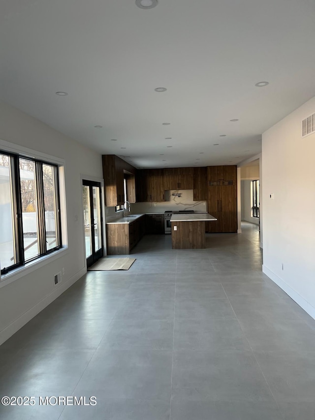 kitchen with a center island, light countertops, a sink, concrete floors, and baseboards