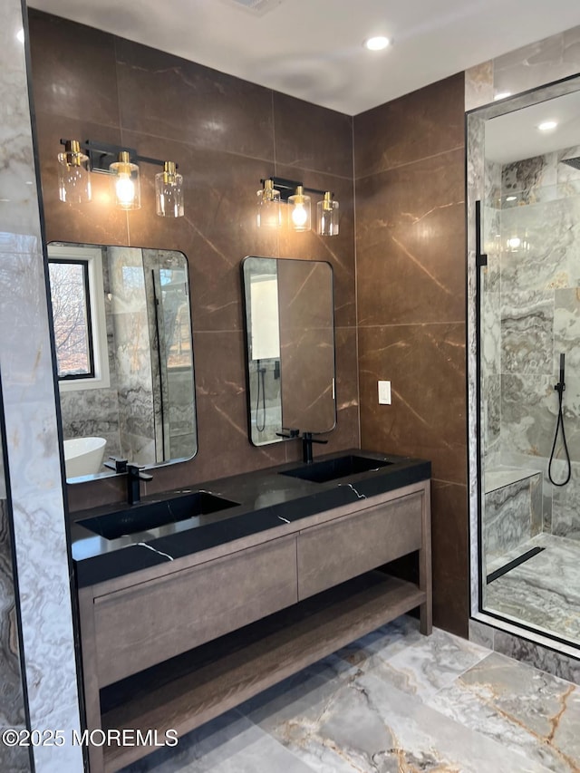 full bathroom with marble finish floor, tile walls, double vanity, a sink, and a shower stall