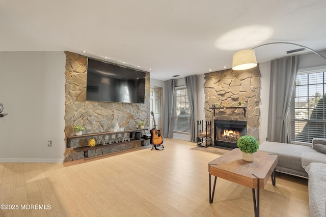 living room with a stone fireplace, wood finished floors, and a healthy amount of sunlight