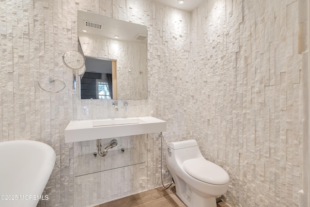 bathroom with visible vents, a freestanding tub, toilet, and tile walls