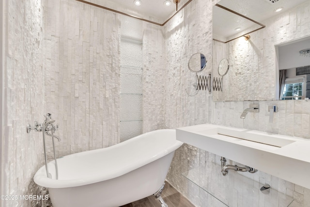 full bath featuring a sink, a freestanding tub, and tile walls