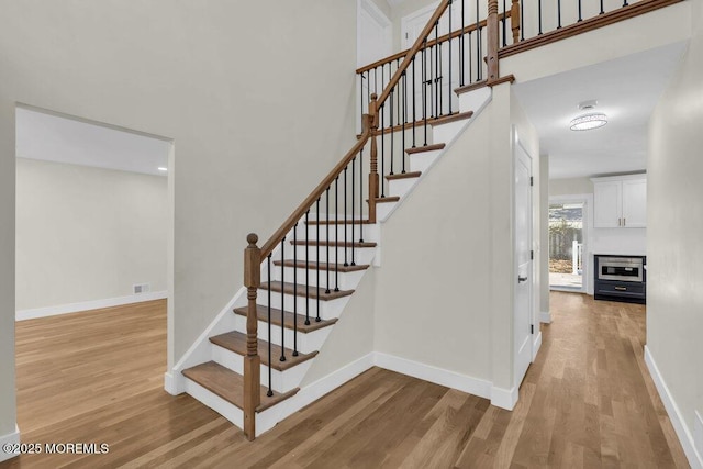 staircase featuring visible vents, a high ceiling, baseboards, and wood finished floors