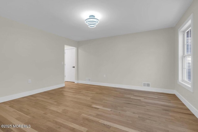 empty room with light wood-style floors, baseboards, and visible vents