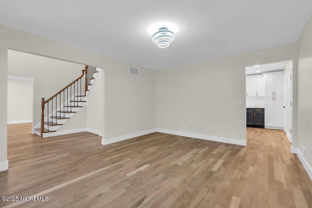 empty room with visible vents, light wood-style flooring, baseboards, and stairs