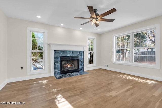 unfurnished living room featuring a premium fireplace, wood finished floors, a wealth of natural light, and baseboards