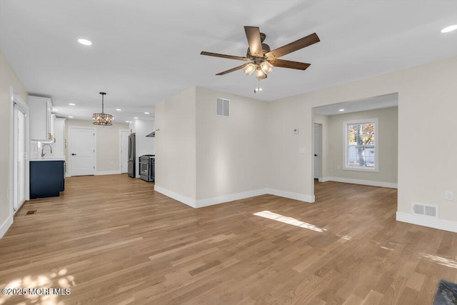 unfurnished living room with light wood-style floors, visible vents, baseboards, and ceiling fan with notable chandelier