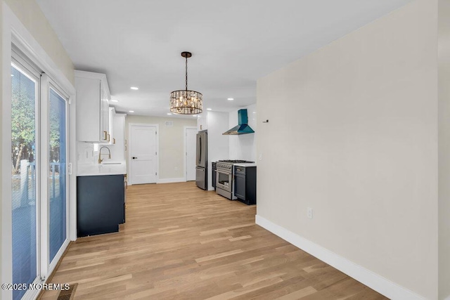 kitchen featuring light countertops, light wood-style flooring, appliances with stainless steel finishes, wall chimney range hood, and baseboards