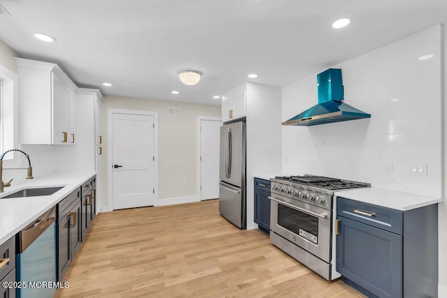 kitchen featuring wall chimney exhaust hood, light wood-style flooring, stainless steel appliances, white cabinetry, and a sink