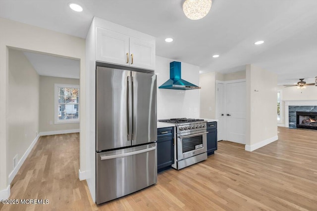 kitchen featuring blue cabinetry, stainless steel appliances, a high end fireplace, white cabinetry, and wall chimney range hood