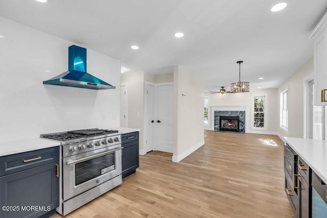 kitchen with a fireplace, light wood-style floors, light countertops, wall chimney range hood, and high end stainless steel range