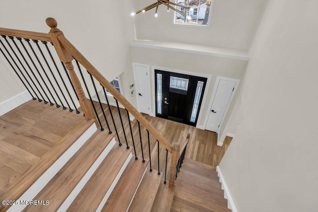 foyer with a notable chandelier, a towering ceiling, wood finished floors, baseboards, and stairs