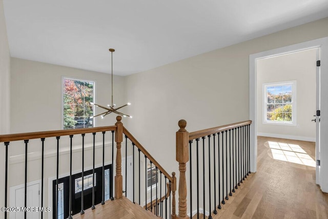 hall featuring baseboards, light wood-style floors, an upstairs landing, and an inviting chandelier