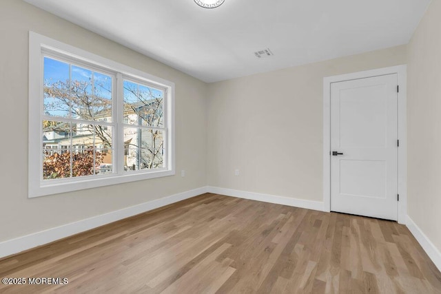 unfurnished room featuring light wood finished floors, visible vents, and baseboards