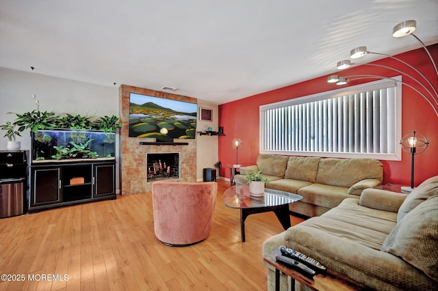 living room with wood-type flooring, visible vents, and a tiled fireplace