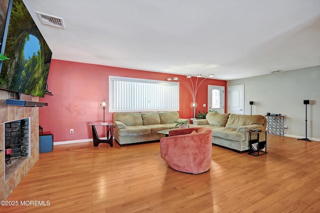 living room with baseboards, visible vents, a tiled fireplace, and hardwood / wood-style flooring