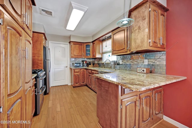 kitchen with stainless steel appliances, a peninsula, a sink, visible vents, and brown cabinetry