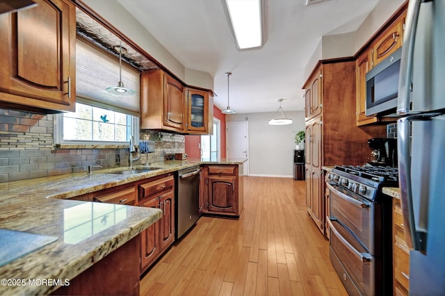 kitchen with light stone counters, stainless steel appliances, a peninsula, hanging light fixtures, and brown cabinets