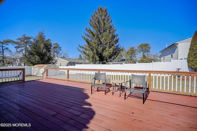 deck with a fenced backyard, an outdoor structure, and a shed