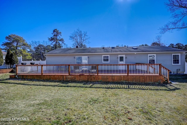 rear view of house with a lawn, a wooden deck, and fence