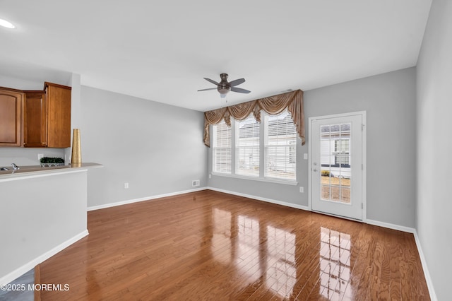 unfurnished living room with a ceiling fan, baseboards, and wood finished floors