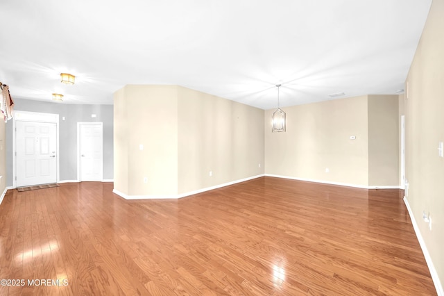 empty room featuring light wood finished floors, baseboards, and a chandelier