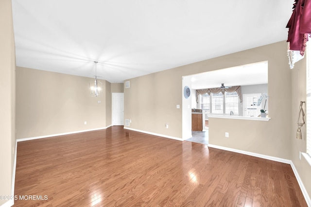 empty room with ceiling fan with notable chandelier, wood finished floors, visible vents, and baseboards