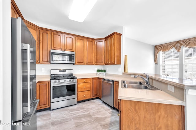 kitchen featuring a peninsula, a sink, light countertops, appliances with stainless steel finishes, and brown cabinetry